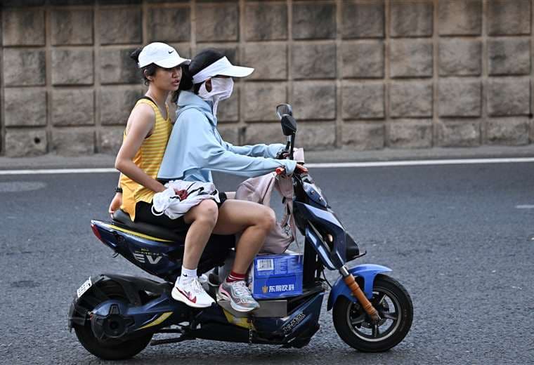 Mujeres viajan en moto durante un día caluroso en Wuhan, China / AFP