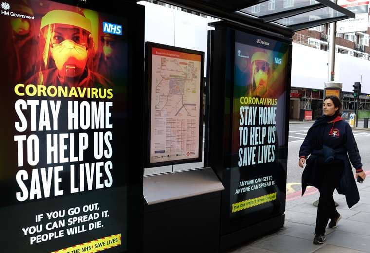 Una mujer cruza delante de carteles sobre el coronavirus en Londres, en una jornada de cierre nacional. Foto AFP