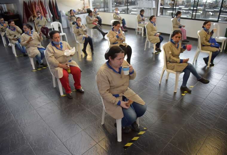 Empleados de una fábrica de artículos de cuero toman su refrigerio manteniendo el distanciamiento social en Bogotá. Foto AFP