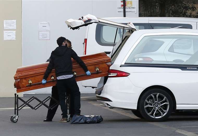 Empleados de una funeraria sacan el ataúd con un fallecido por coronavirus del hospital San José de Santiago. Foto AFP