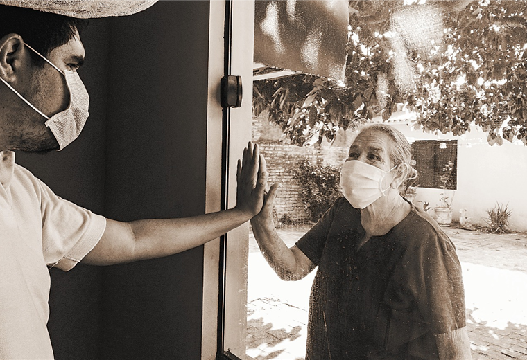 Jorge y su abuelita Miriam unen sus manos mediante cristal. Foto. Jorge Ibáñez  