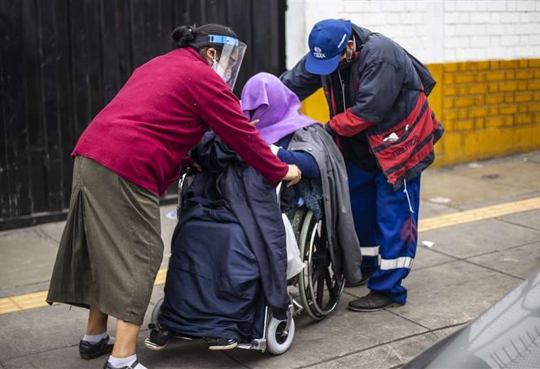 Familiares ayudan a una señora en silla de ruedas enferma de Covid-19 fuera de un hospital de Lima. Foto AFP