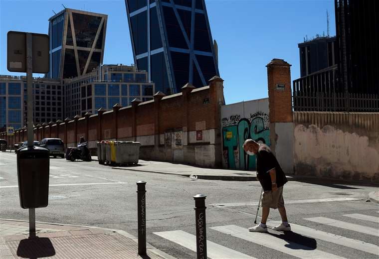 Un anciano con mascarilla camina por Madrid, con la Puerta de Europa (Torres Kio) al fondo. Foto AFP