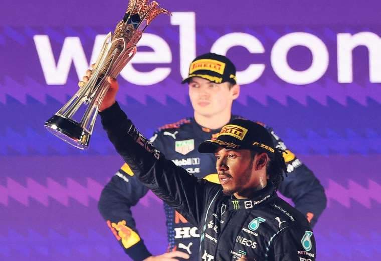 Hamilton con el trofeo en manos y el rostro de Verstappen lo dice todo. Foto: AFP